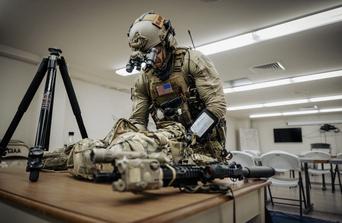Service member in field equipment beside a laid-out operational kit.